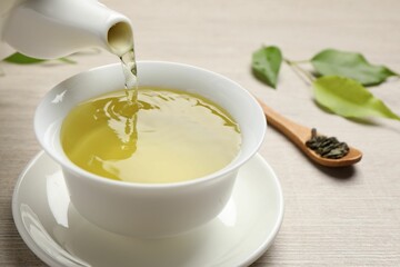 Pouring refreshing green tea into cup at wooden table, closeup