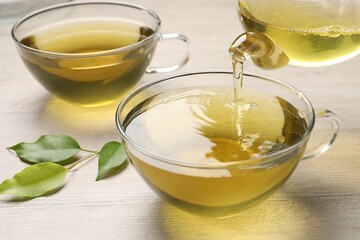 Pouring refreshing green tea into cup at wooden table, closeup