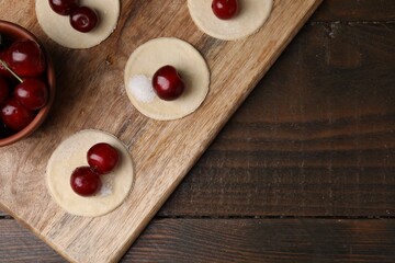 Process of making dumplings (varenyky) with cherries. Raw dough and ingredients on wooden table, top view. Space for text
