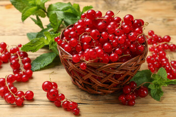 Fresh red currants in basket and mint on wooden table, closeup