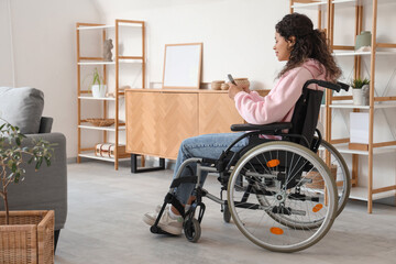 Young African-American woman in wheelchair with mobile phone at home