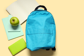 Backpack with green apple and notebooks on yellow background. Top view