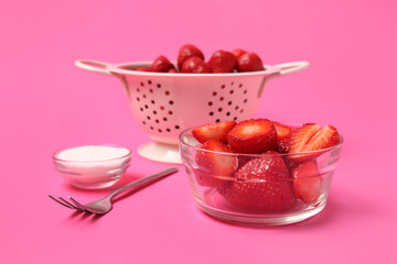 Glass bowl and colander with fresh sweet strawberries on pink background