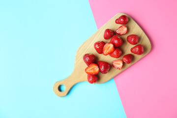 Wooden board with fresh sweet strawberries on colorful background