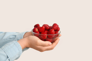 Female hands with glass bowl of sweet fresh strawberries on grey background