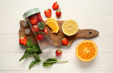 Sports bottle of infused water with strawberries, lemon and mint on white wooden background