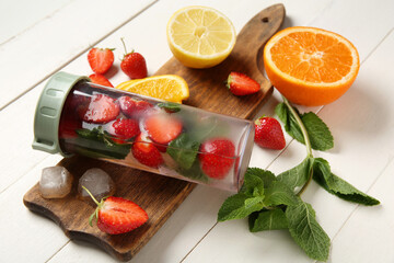 Sports bottle of infused water with strawberries, lemon and mint on white wooden background