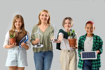 Pupils with teacher holding wind turbine models and portable solar panels on light background....