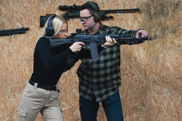 A shooting instructor teaches a young girl of European appearance to shoot with an AK rifle at a...