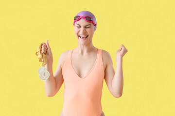 Happy young female swimmer with first place medals celebrating success on yellow background