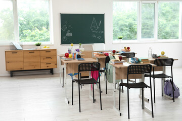 Desks with apples and school stationery in empty classroom