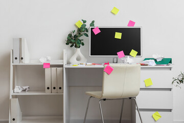 Messy workplace with computer monitor and sticky notes in light office