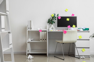 Messy workplace with computer monitor and sticky notes in light office