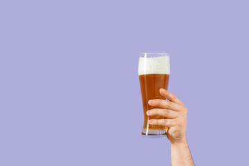 Hand with glass of beer on lilac background