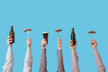 Hands with beer and sausages on blue background