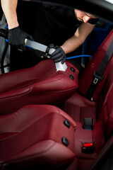 Cleaning car backseat with special vacuum nozzle. Detailing car seats with the help of vacuum extractor.