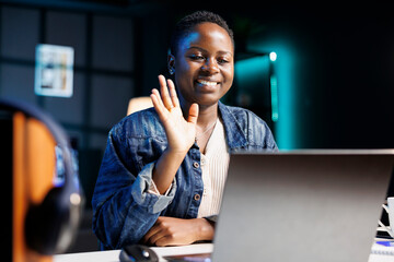 African american student waving towards laptop screen, making video call with fellow colleagues. Female freelancer seated in apartment having online conference call with clients on personal computer.