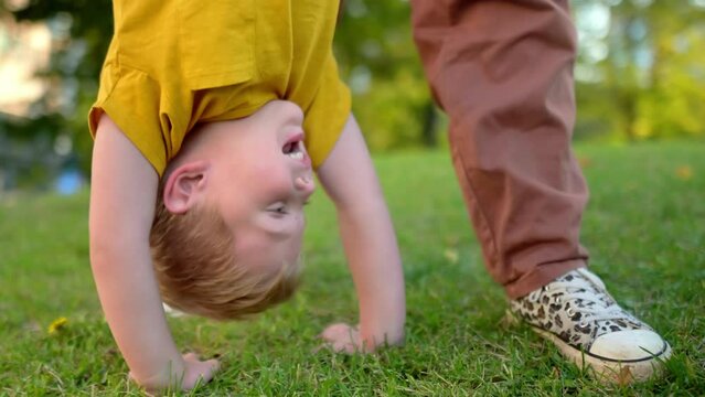 Mom and her little son are having fun together in a city park on a warm summer evening. Active family. Mom swings happy laughing boy upside down. Quality time and activity for mom and her child