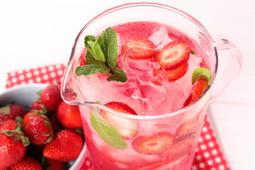 Freshly made strawberry lemonade with mint in jug on white wooden table, closeup