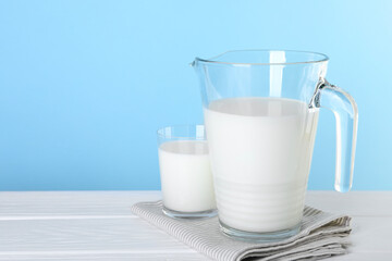 Jug and glass of fresh milk on white wooden table, space for text