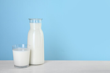 Carafe and glass of fresh milk on table against light blue background, space for text