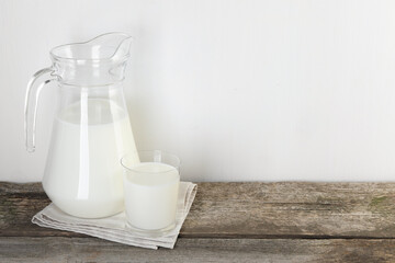 Jug and glass of fresh milk on wooden table, space for text