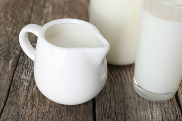 Jug of fresh milk and glass on wooden table, closeup