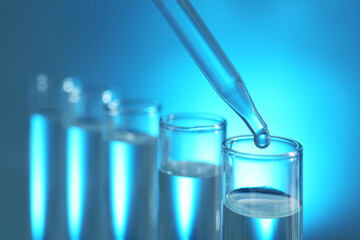 Dripping liquid from pipette into test tube on light background, closeup