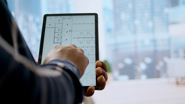 Financier realtor and client examining blueprints on a tablet and establishing the renovation plans before reaching an agreement. Businessman planning an investment during office tour. Camera A. - Powered by Adobe