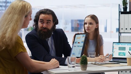Financial advisor showing statistical graphs on tablet to clients, analyzing market trends to optimize their income. Mother and daughter checking investment plan on device, camera B