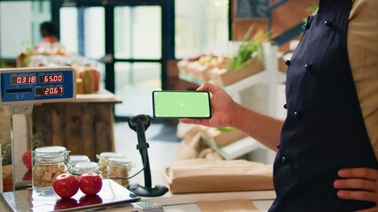Merchant with phone greenscreen at store counter, presenting isolated chromakey display on mobile gadget. Farmer and vendor using modern copyspace template with mockup technology.