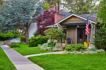 Charming Suburban Home with American Flag and Sprinkler in Motion