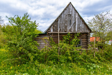 Obraz premium The facade of an abandoned wooden house with windows. The old residential architecture is destroyed and abandoned. A log wall with windows and a roof.