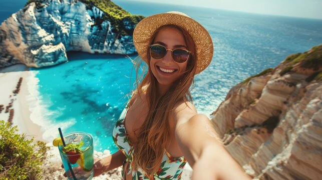 A woman sipses on a cocktail and takes a selfie against the gorgeous Greek beach. - Powered by Adobe