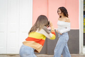 Woman photographer taking pictures of her friend posing outdoors