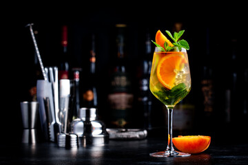 Summer sangria cocktail with white wine, peach, orange, lime and ice. Black background with bottles