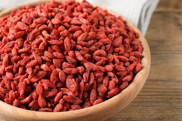 Dried goji berries in bowl on wooden table, closeup