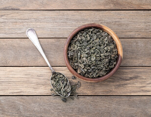 Dried green tea leaves on a bowl over wooden table