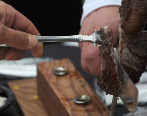 Close-up of hands cutting a piece of grilled meat with a knife and fork