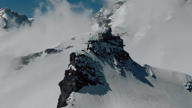 Aerial orbit right to establish backlit sphinx observatory in Jungfraujoch Switzerland, white clouds and snow in background