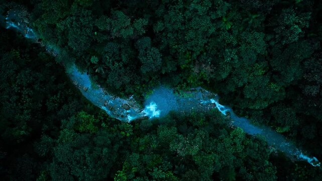 Aerial Top Down view of vivid blue river with waterfall flowing in lush rainforest