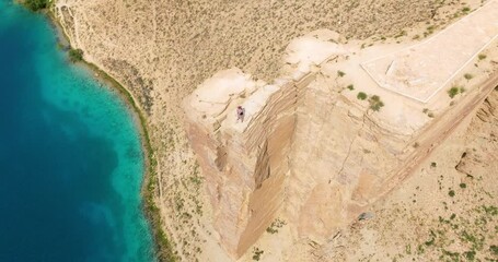 Man Standing On Top Of Cliff Overlooking Blue Lake At Band-e Amir National Park In Bamyan, Afghanistan. aerial orbiting shot