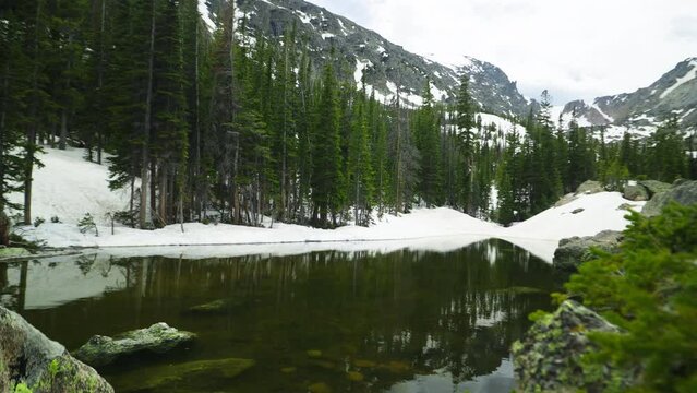 Slow push, revealing Lake Haiyaha, the Rocky Mountain scenery with the green forest, the blue sky, the unmelted snow and the mountain in the background