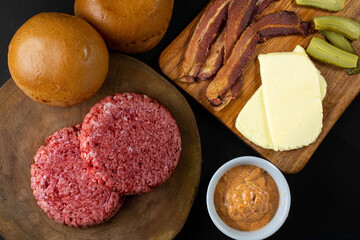 Ingredients for cooking burgers. Raw ground beef meat cutlets on wooden chopping board, cheese, bacon, over wooden background - Top View