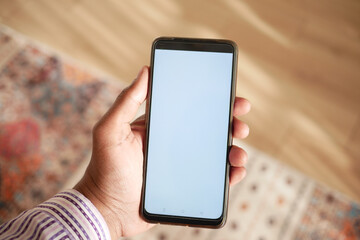 holding smart phone with empty screen and home interior decoration on table 