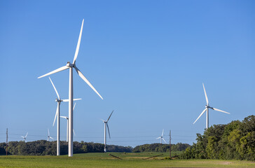 Fototapeta premium Landscape view of gigantic wind turbines in an agricultural field under clear blue sky, with copy space