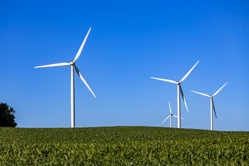 Landscape view of gigantic wind turbines in an agricultural field under clear blue sky, with copy...