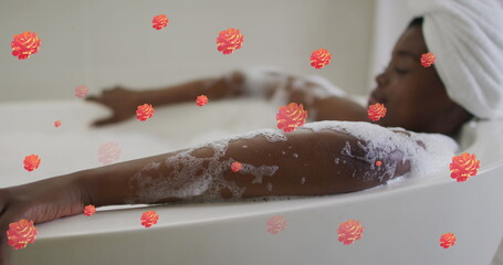 Image of flower icons over african american woman taking bath