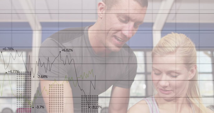 Image of graphs and numbers on caucasian male trainer helping woman in dumbbells exercise in gym