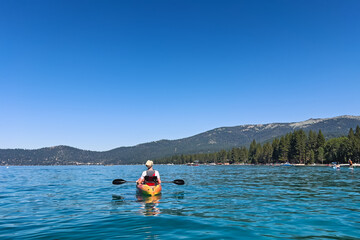 A person kayaking on a calm, clear blue lake with mountains in the background